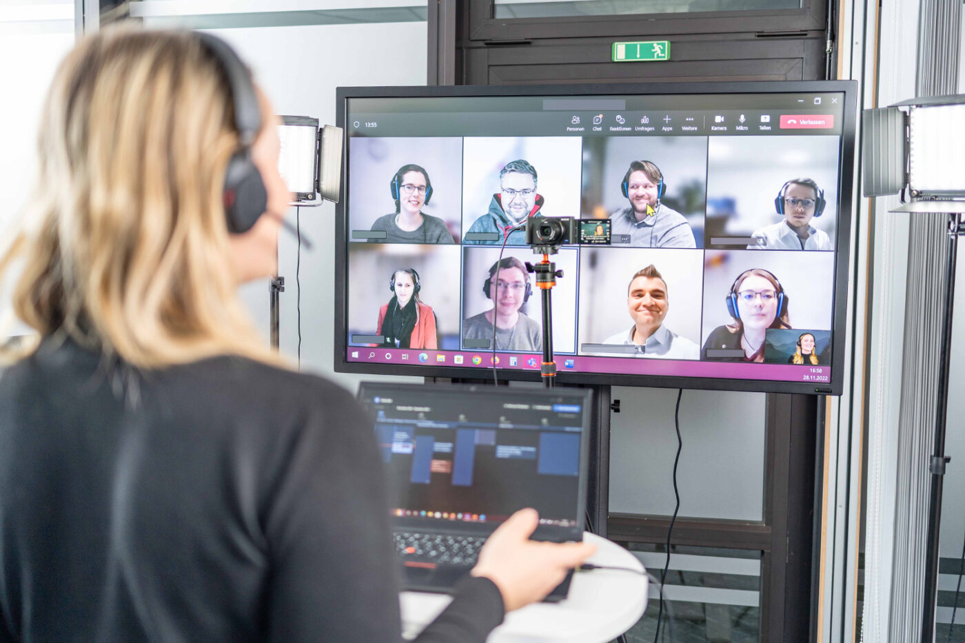 Trainerin Pia Krone steht mit einem Headset vor ihrem Computer und einer Kamera. Sie gibt eine Remote Schulung im Rahmen des BREDEX Academy Programms.