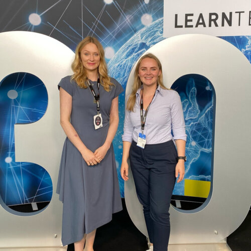 Pia Krone, Learning & Development Specialist bei BREDEX, eine weiße, blonde, junge Frau steht vor einem großen silbernen 30. Im Hintergrund ist das Logo der LearnTec abgebildet.